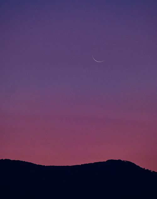 Free A crescent moon setting over a mountain silhouette against a purple twilight sky in Tirana, Albania. Stock Photo