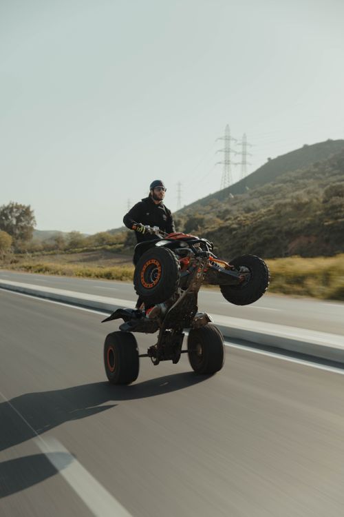Free Man performing a wheelie on an ATV on a clear road, showcasing adventure and skill. Stock Photo