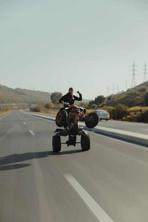 Free Stunt rider performs wheelie on off-road vehicle on a highway, showcasing daring skill. Stock Photo