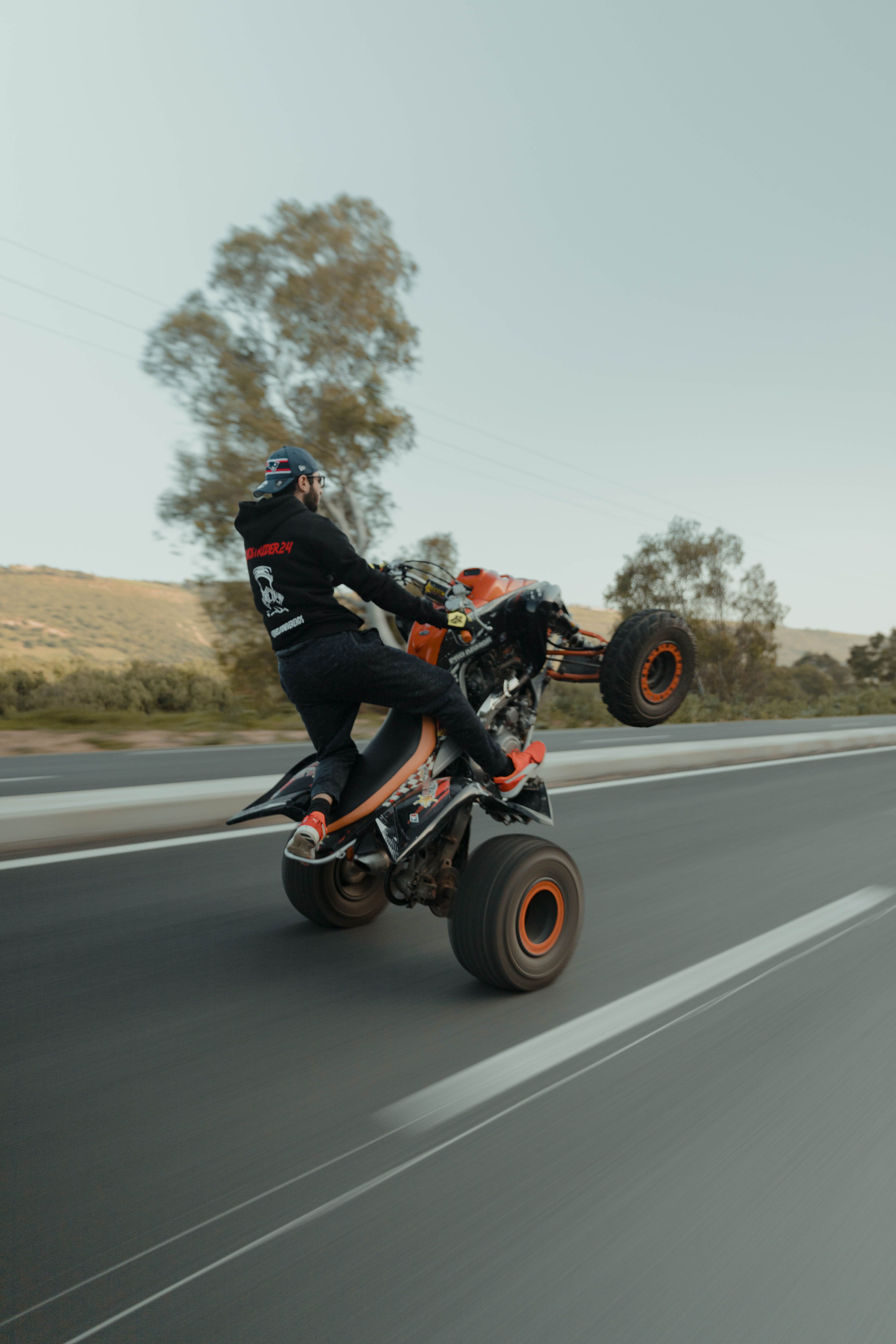 Man performing an ATV stunt on the open road, showcasing skill and speed.