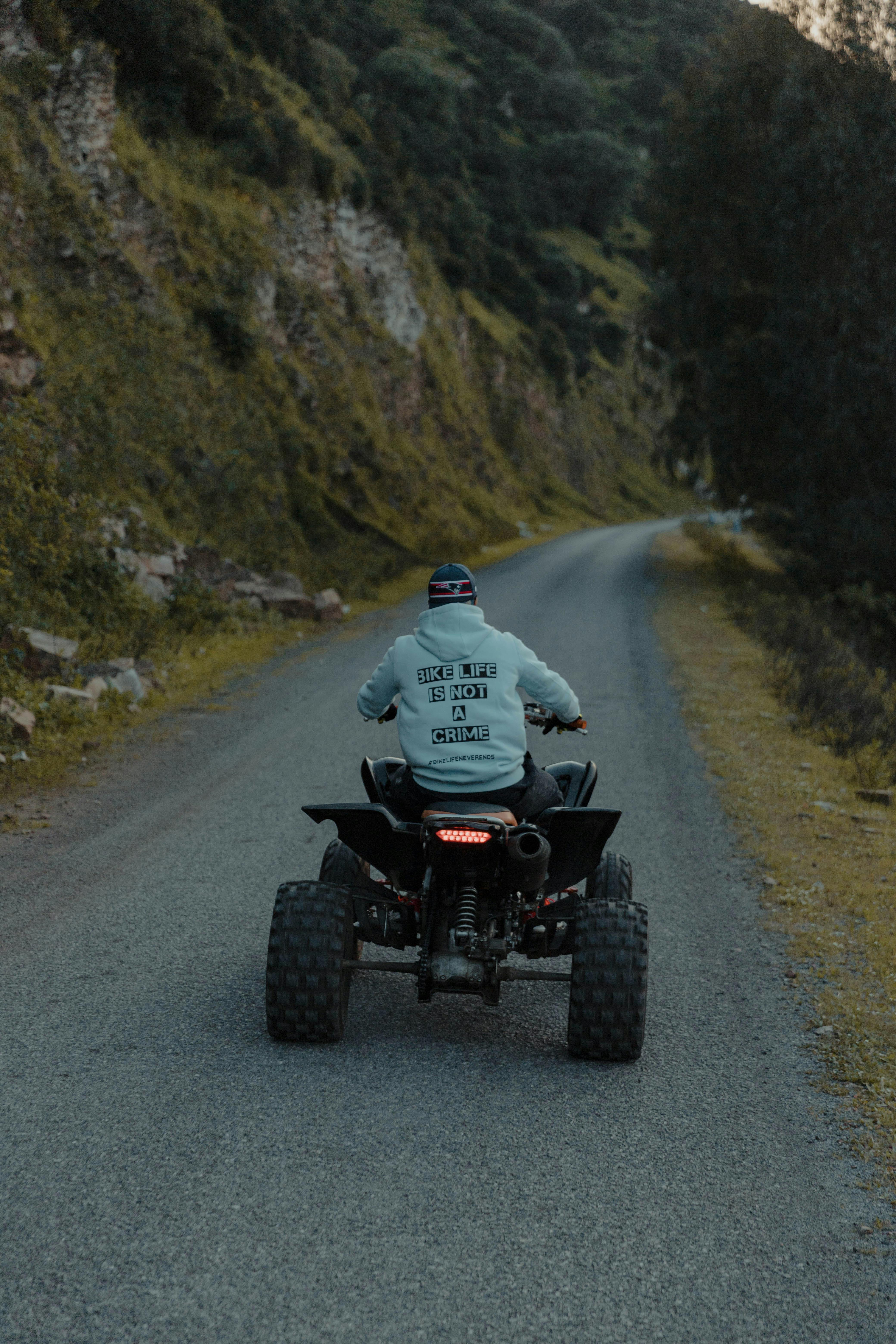 A man rides an ATV down a narrow, scenic path bordered by foliage.
