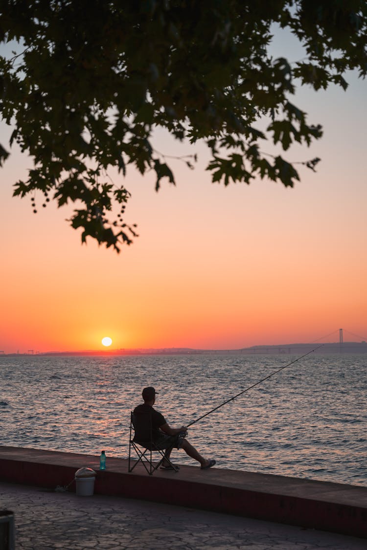 Silhouette Of A Man Fishing While Sitting On A Chair