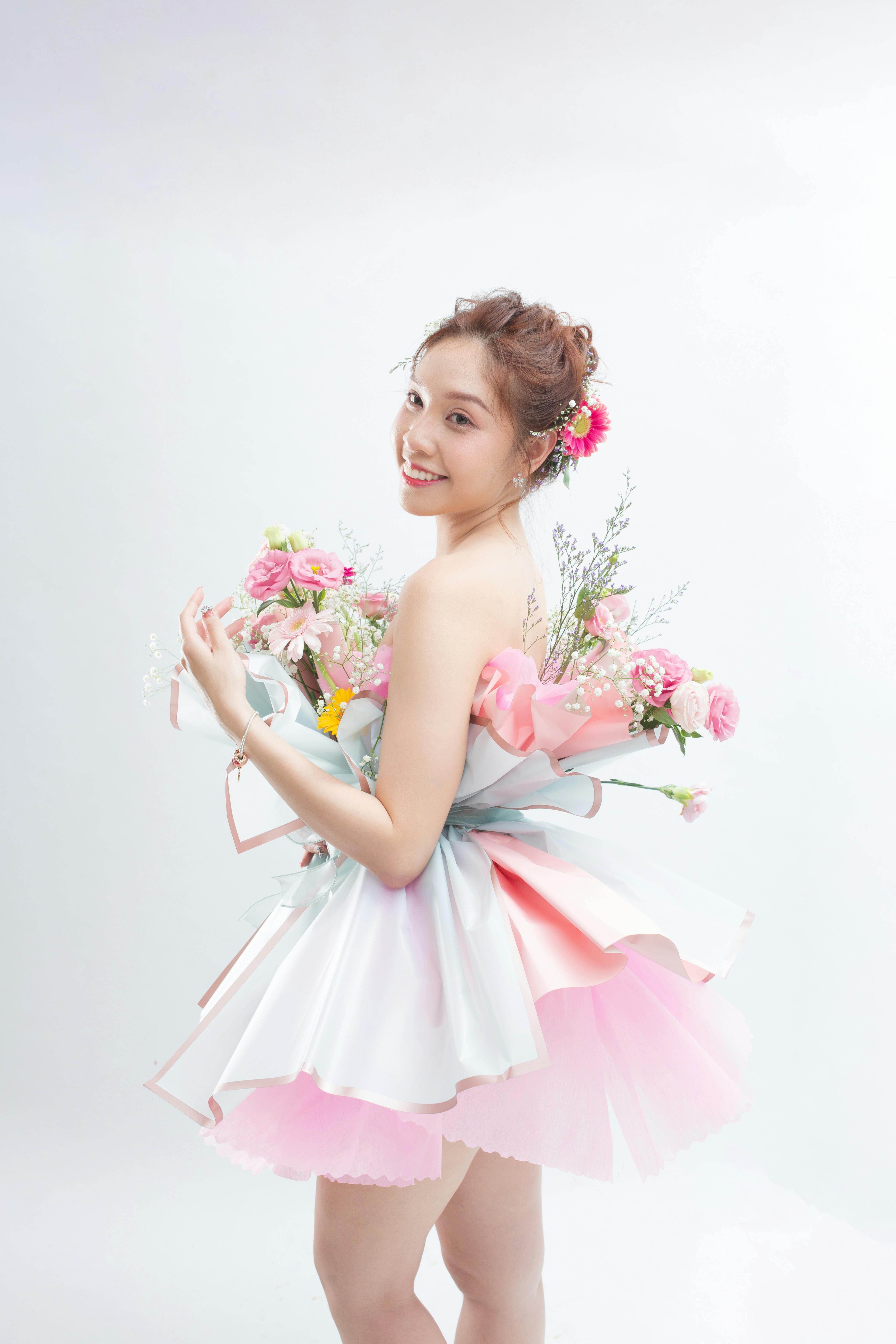 A beautiful woman in a floral dress poses gracefully against a white background.