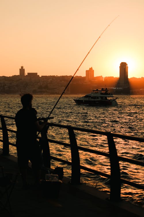 Silhouette of Person Standing on Dock with Fishing Rod during Sunset