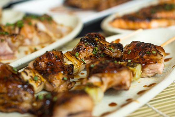 Glazed chicken and scallion yakitori skewers with sliced green onion on white plates