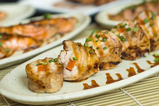 Delicious grilled sushi rolls garnished with green onion and sauce on ceramic plate.