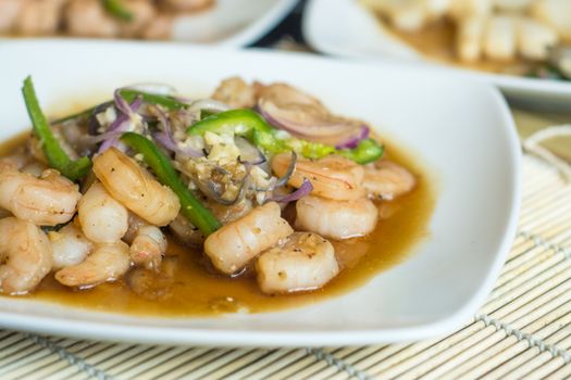 Close-up of seasoned shrimp with green peppers and onions in sauce on a white plate.