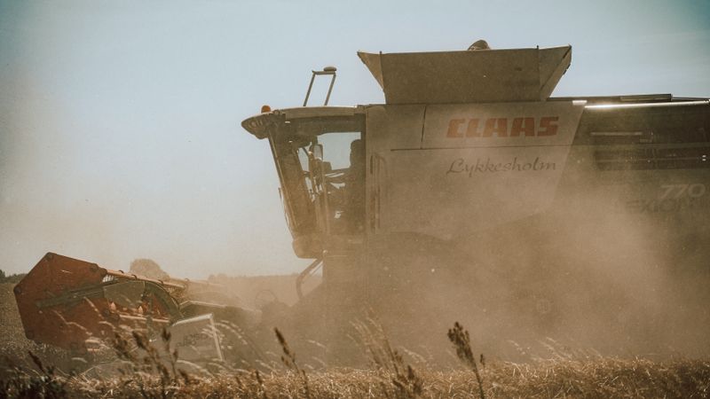 Side view of a combine harvester working in a dusty wheat field