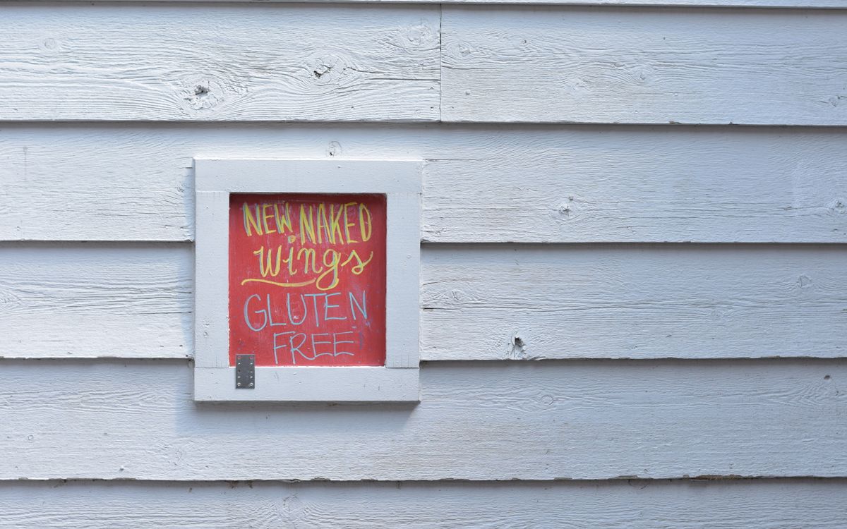 A colorful sign advertising gluten-free wings displayed on a white wooden wall.