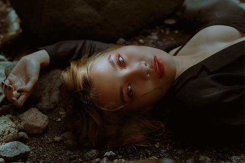 Free A woman in a black blazer lies on rocky ground, exuding mystery and allure. Stock Photo