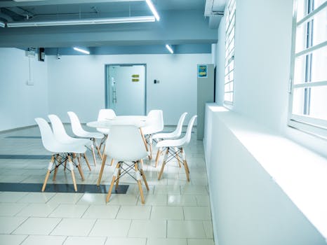 A clean and minimalistic office meeting room with white chairs and table.