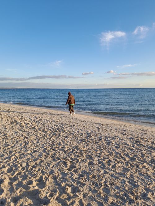 Free An adult walks along the serene shores of Chelsea Beach, Victoria, Australia, at sunset. Stock Photo