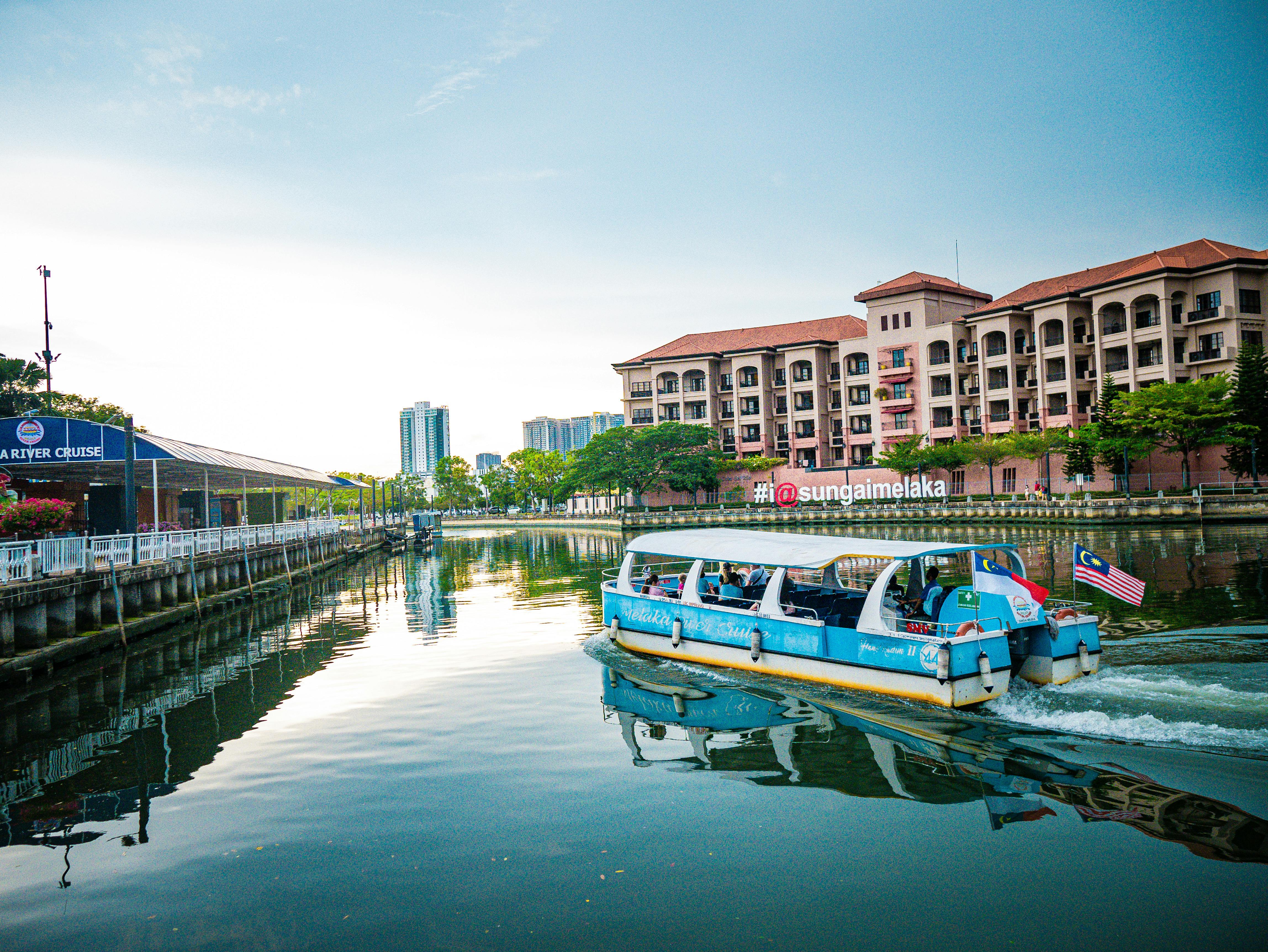 Colorful boat cruising on Melaka River with scenic view of buildings and blue sky. - ¿Dónde dormir en Melaka?