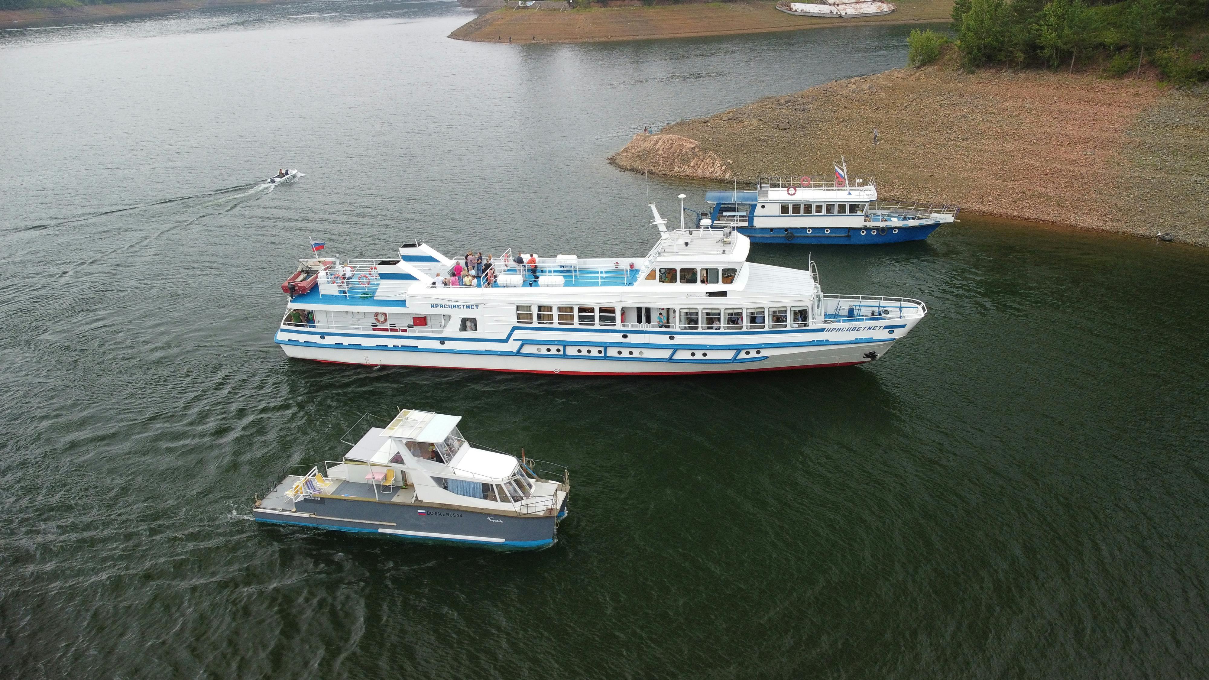Free Drone captures ferry boats navigating the calm waters of Divnogorsk, Russia, showcasing serene landscape and transportation. Stock Photo