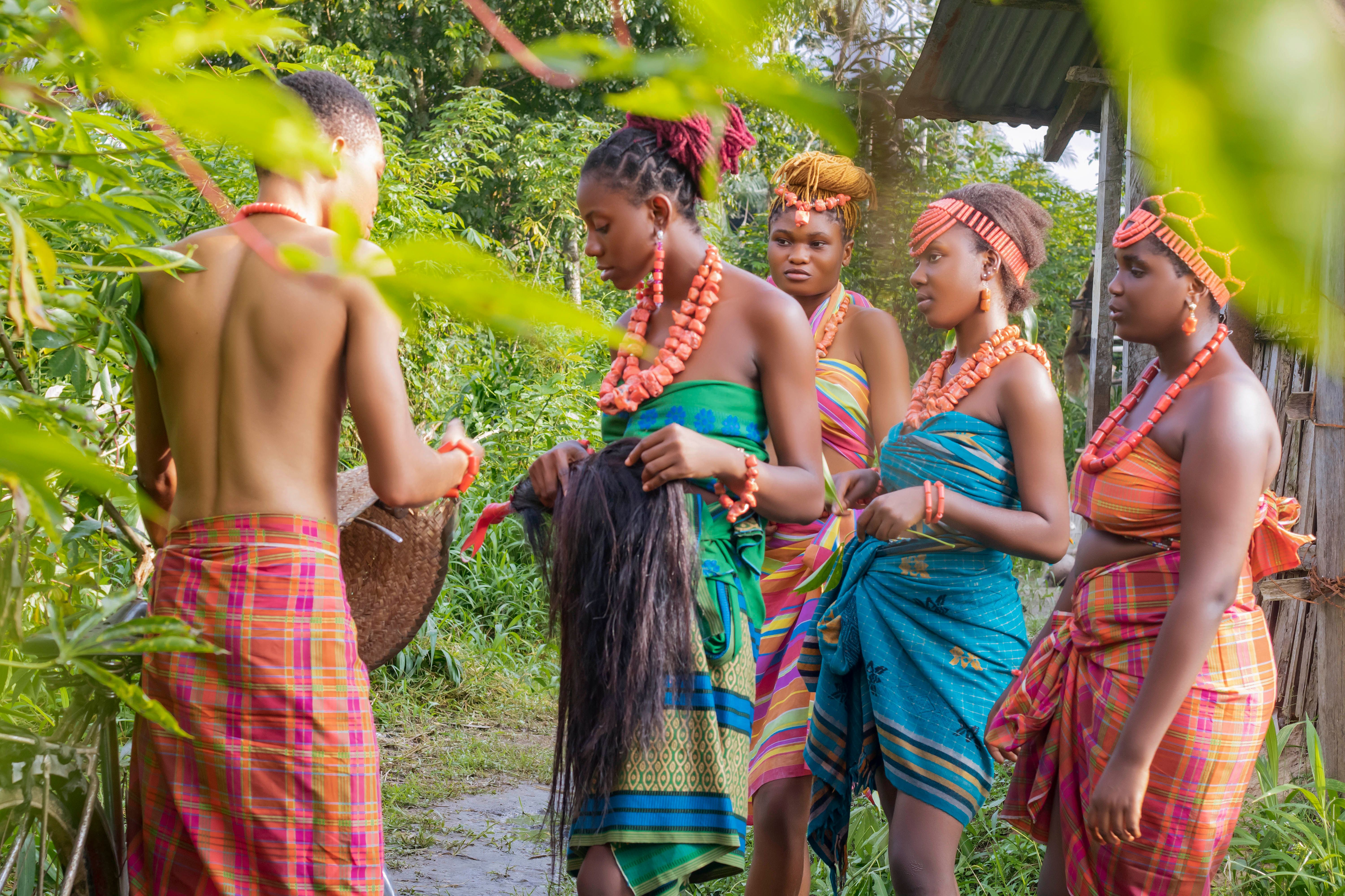 A group of African adults in colorful traditional dresses gathered outdoors in a natural setting.