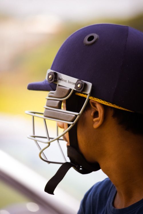 Free Side view of a young cricket player wearing a helmet, focused and ready for the game. Stock Photo