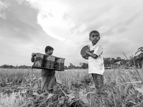 Two boys with pails and baskets playing in a grassy field under a cloudy sky.