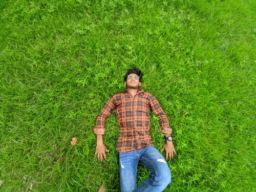 Free A young man in sunglasses and plaid shirt relaxes on a lush green grass field in Bangladesh. Stock Photo