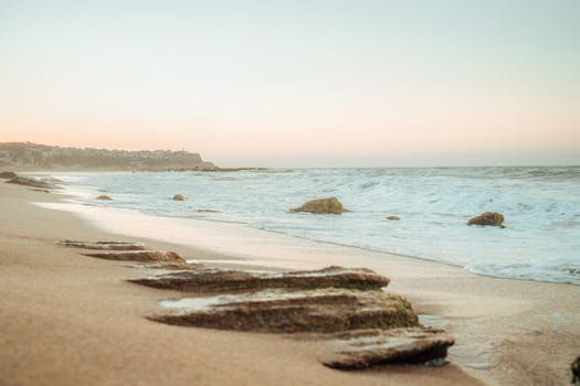 Serene sandy beach at sunrise with gentle waves and distant cliffs.