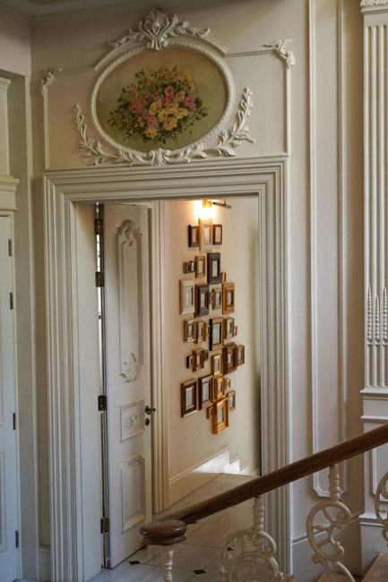 Ornate white door leading to a hallway adorned with vintage picture frames.