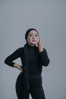 Portrait of a confident woman wearing a black outfit and headscarf against a gray background.