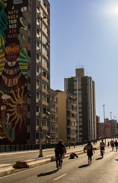 Free Vibrant street mural scene with cyclists in São Paulo's urban landscape amid bright sunlight. Stock Photo