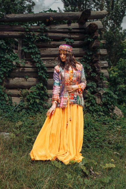 A woman in vibrant traditional attire standing outside a rustic wooden structure.