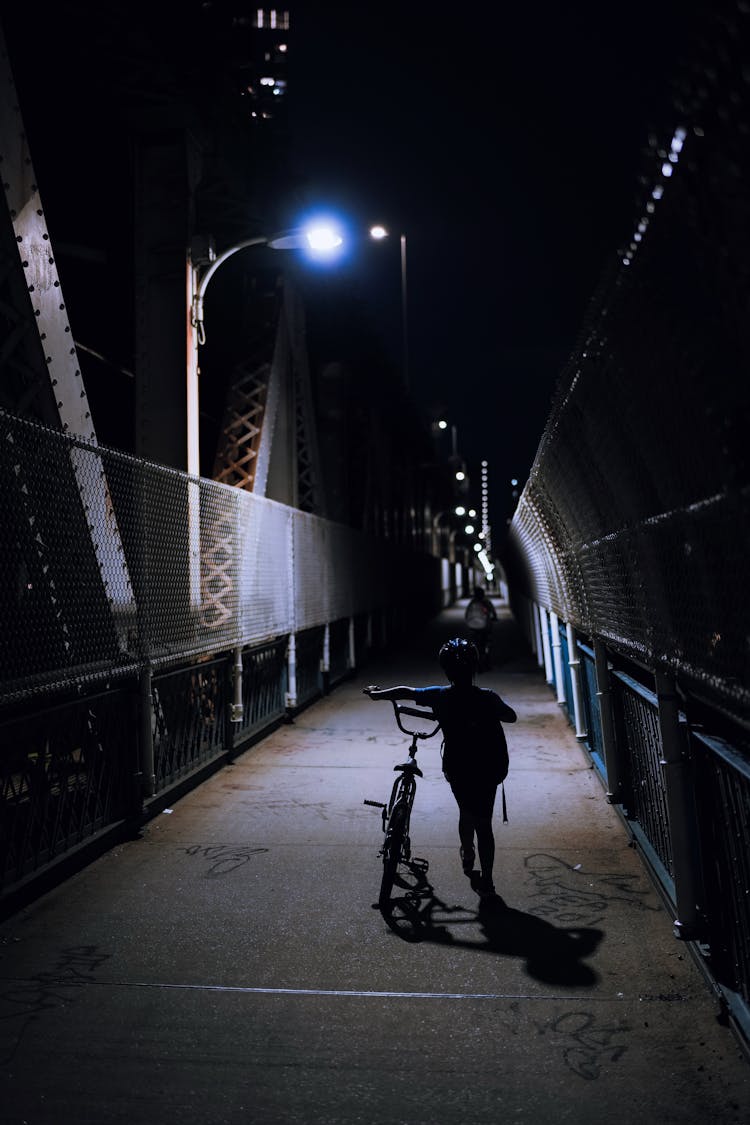 Silhouette Of A Kid Pushing His Bike On A Bridge 