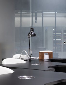 A minimalist office setup featuring a sleek lamp on a black desk with a window view.