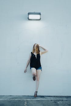 Blonde woman in denim shorts poses against a minimalist wall, creating a modern and artistic vibe.