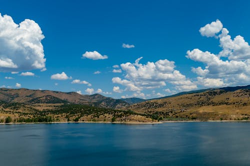Green Trees On Brown Mountains Beside Body of Water Under Blue and Cloudy Sky