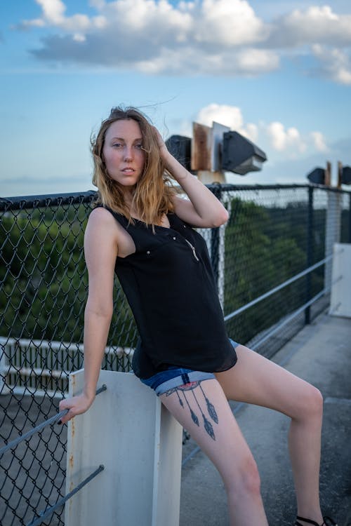 A Woman in Black Tank Top and Shorts Sitting Beside Black Chain Link Fence