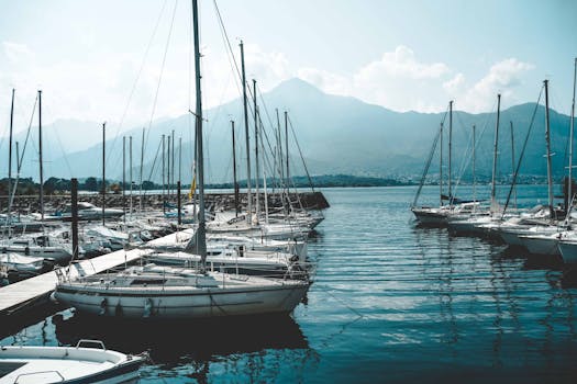 在意大利一个宁静的码头，明亮的天空下，帆船停靠在以山为背景的地方