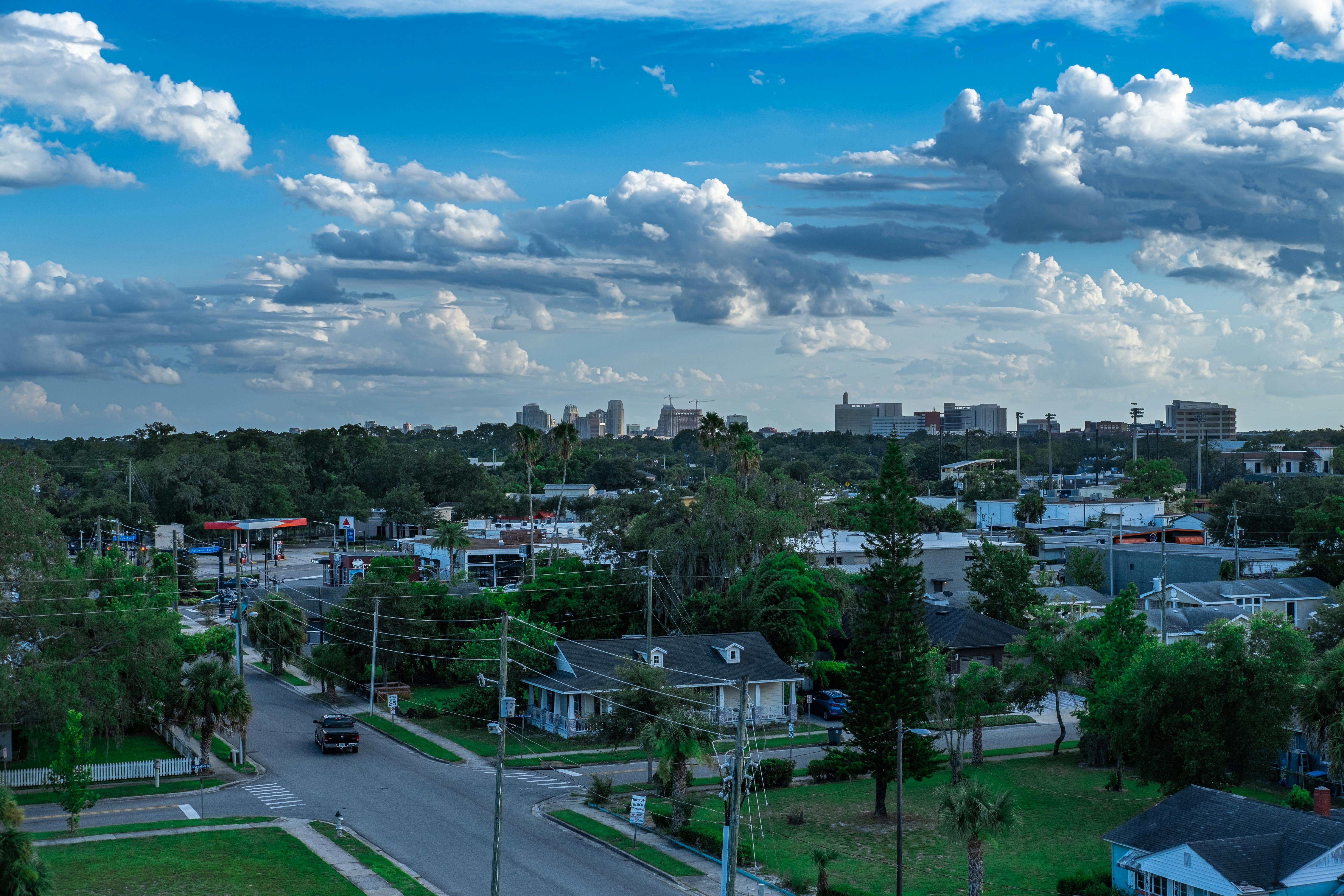 Aerial cityscape showcasing residential neighborhood with lush greenery and a vibrant blue sky.