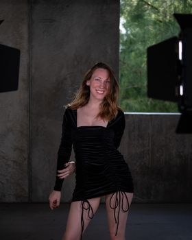 A woman in a stylish black dress poses happily indoors with professional lighting.