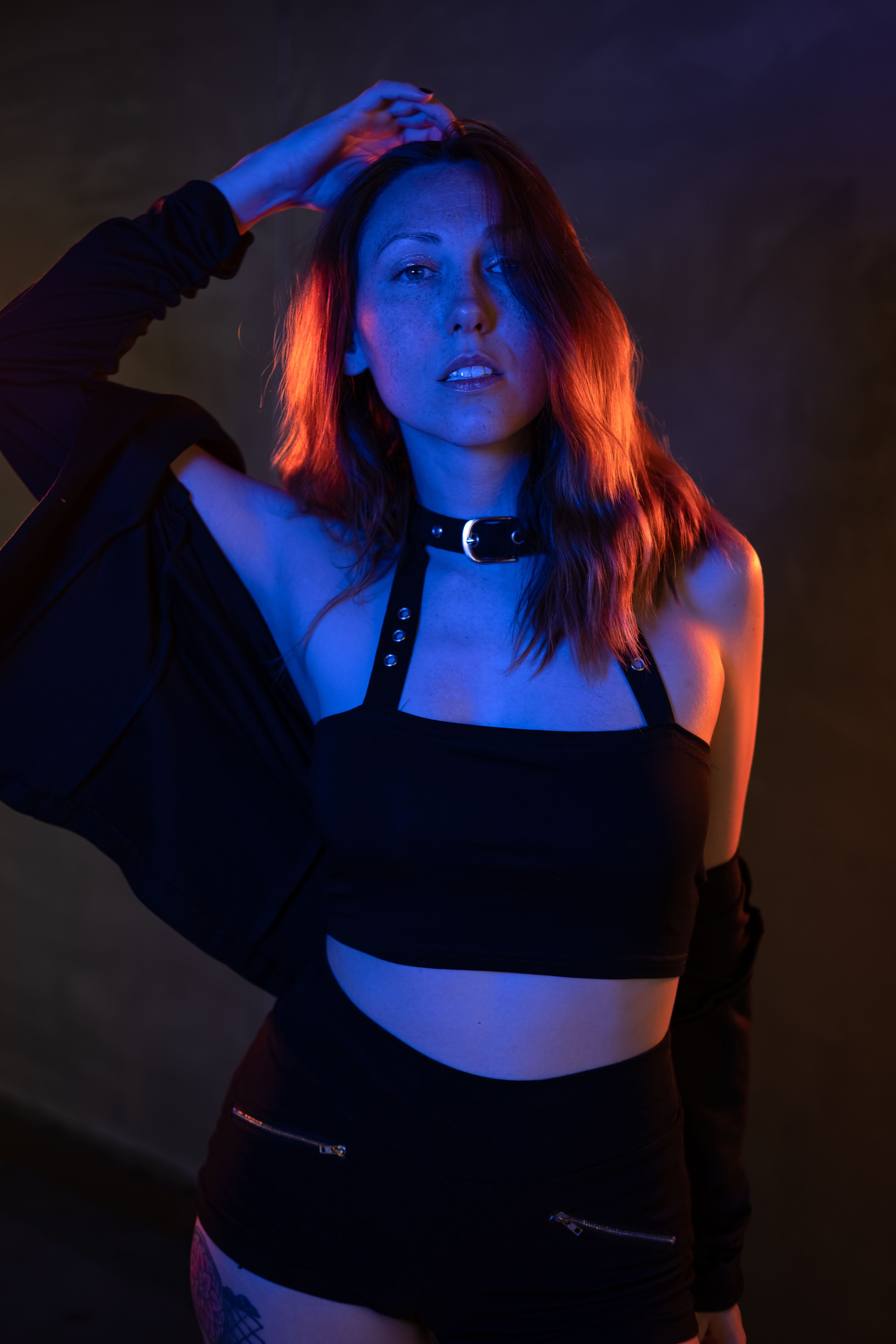A red-haired woman posing in dynamic lighting, highlighting her glamour and style.