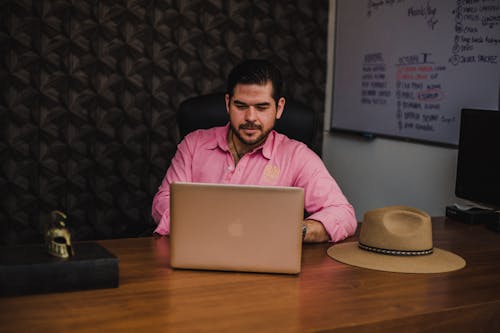 Free Man in Pink Dress Shirt Sitting on Black Chair in Front of Macbook Stock Photo