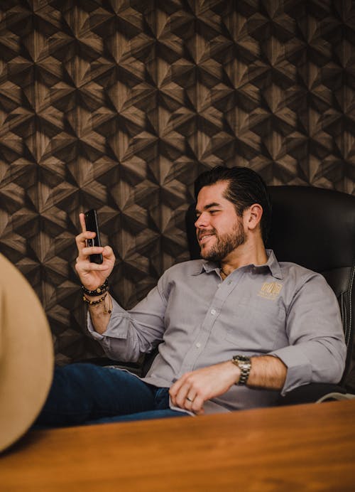 Smiling Man Sitting in Office Using Smartphone