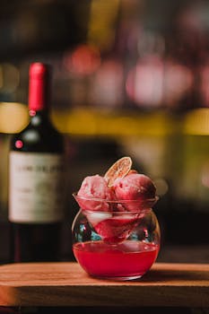 Close-up of a vibrant cocktail with citrus garnish on a wooden table, against a warm bokeh background.