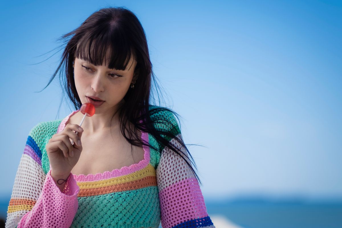 Fashionable young woman with lollipop on a breezy outdoor day, wearing colorful crochet top.