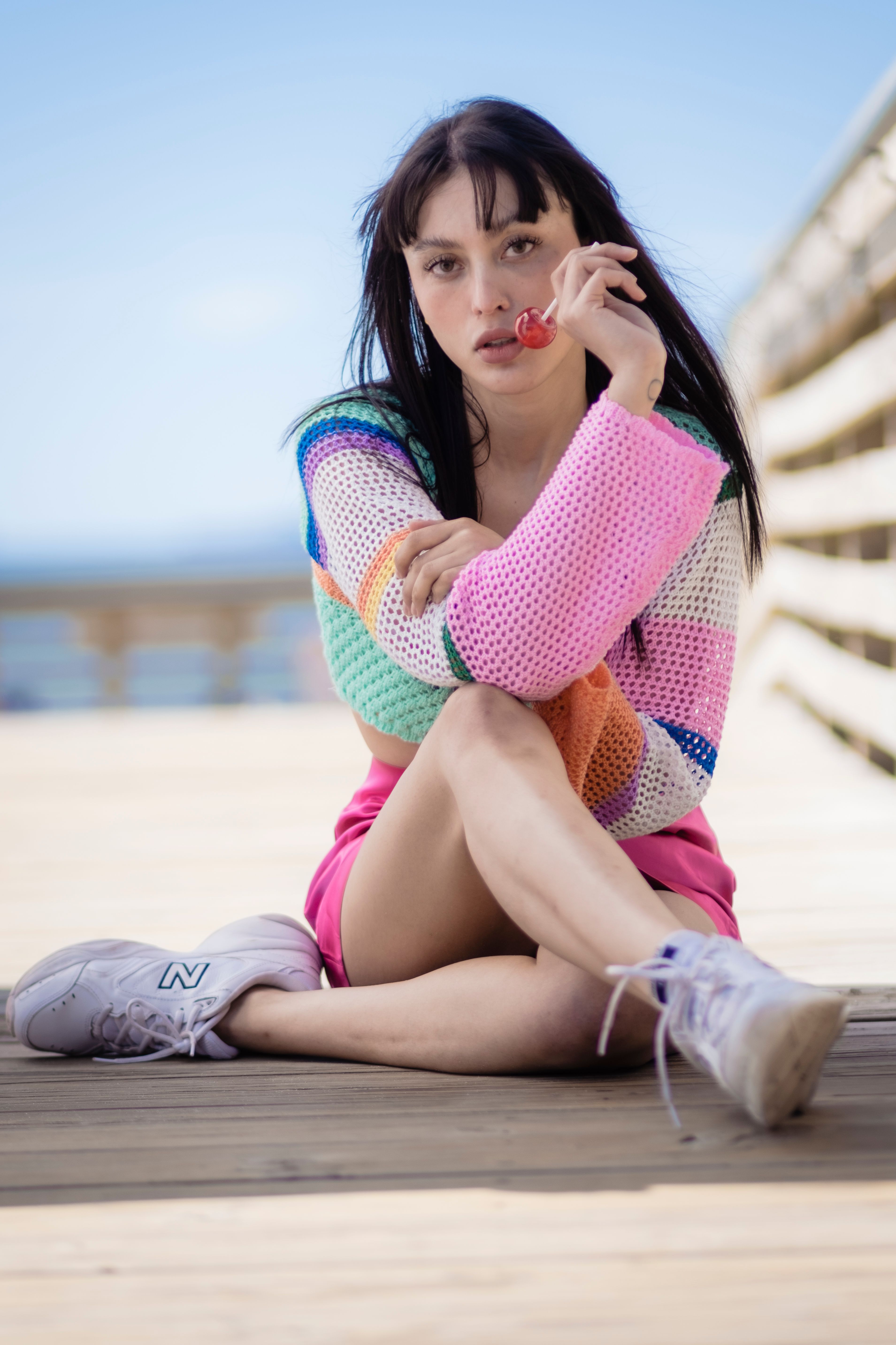 Colorful young woman enjoying a lollipop while sitting on a sunny boardwalk.