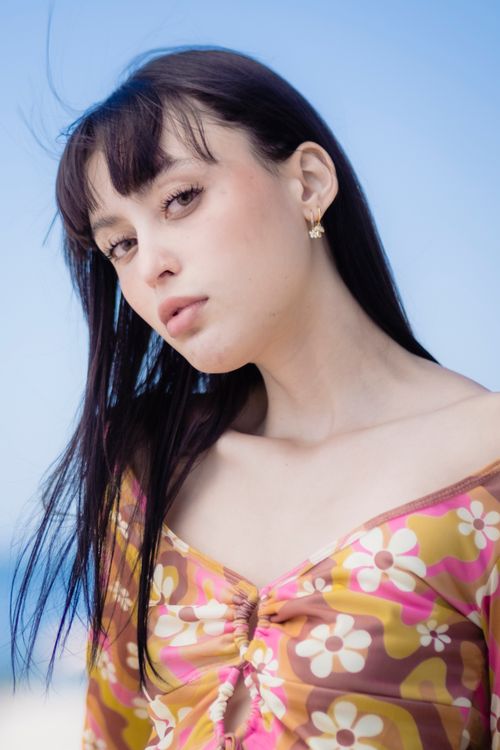 Free Portrait of a woman in a floral top against a blue sky background, exuding elegance and style. Stock Photo