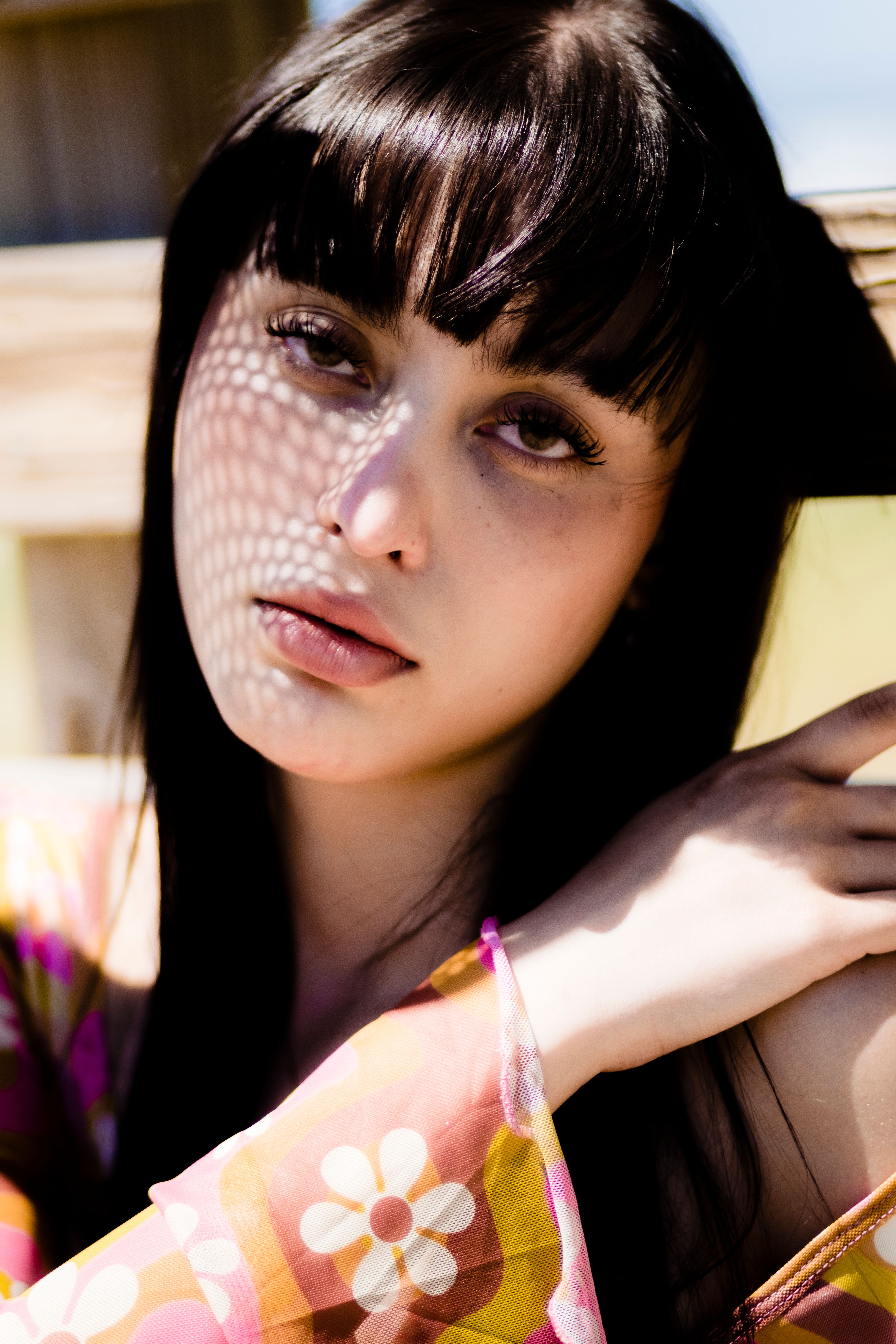 Close-up portrait of a young woman with bangs, sunlight casts floral shadows on her face.