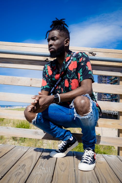 A Man in Printed Shirt Sitting on a Wooden Bridge with His Hands Together