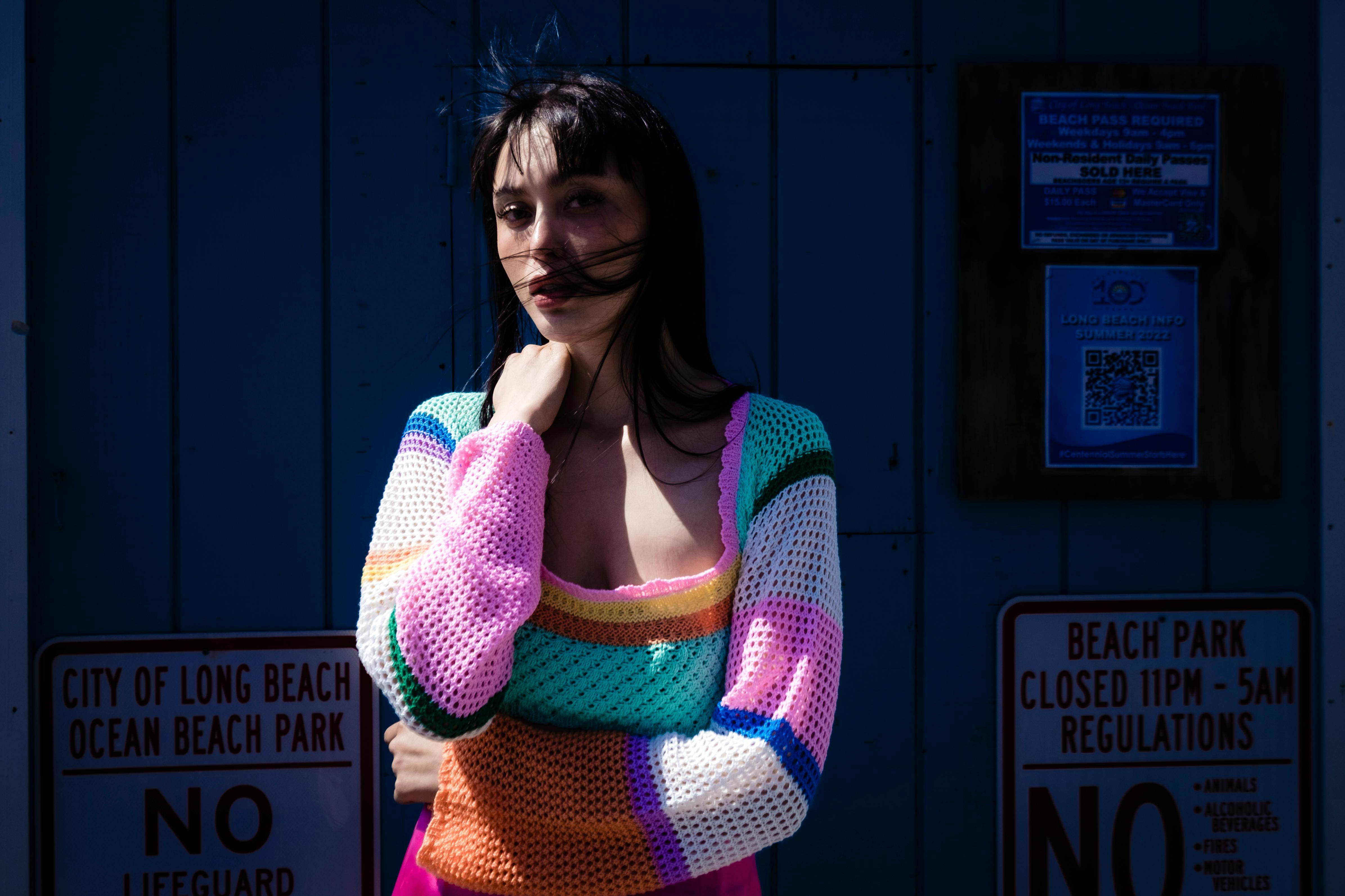 A woman poses in a colorful sweater at Long Beach, blending fashion with coastal vibes.