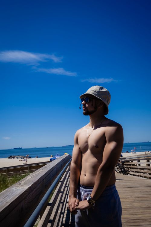 Free Muscular man standing shirtless on a sunny beach boardwalk with clear blue skies. Stock Photo