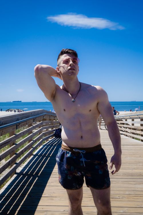 Free Muscular man posing shirtless on a sunny beach boardwalk. Stock Photo
