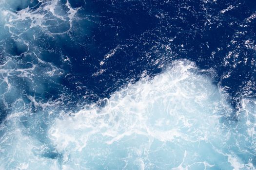 Dynamic aerial view of deep blue ocean waves and frothy seafoam patterns.
