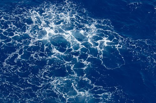 Free Stunning aerial view of ocean waves and seafoam patterns on a bright blue sea. Stock Photo