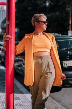 Stylish woman in orange outfit leaning on a red pole, creating a vibrant street style look.